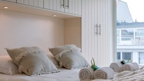 Een hotelkamer met een bed, witte kussens, opgerolde handdoeken en uitzicht op een gebouw door een raam.