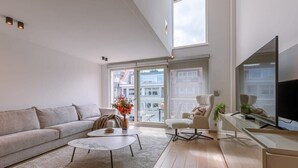 Een moderne woonkamer met een bank, salontafel, fauteuil, een flatscreen-tv en grote ramen met uitzicht op de stad.