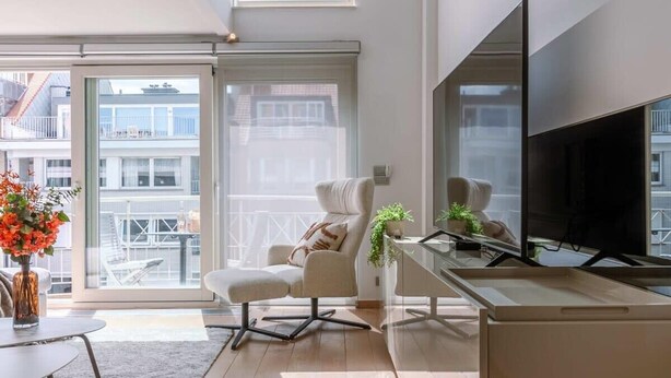 Een moderne woonkamer met een grote televisie, een bank, een salontafel en uitzicht op de stad door grote ramen.