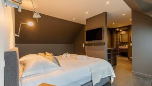 Moderni hotellihuone, jossa on suuri sänky, taulutelevisio, erillinen vaatehuone ja kylpyhuone, jossa on suuri peili.
