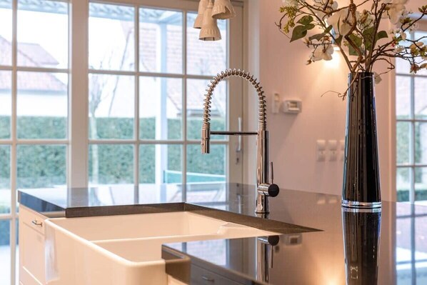 Ein modernes Badezimmer mit einem großen Fenster, einer schwarzen Vase mit Blumen und einem chromfarbenen Wasserhahn.