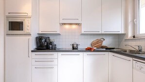 Et moderne køkken med hvide skabe, indbygget ovn, kaffemaskine og skærebræt i træ.