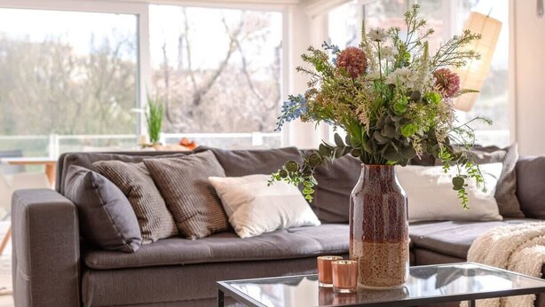 En stue med en sofa, et glasbord og en vase med blomster.