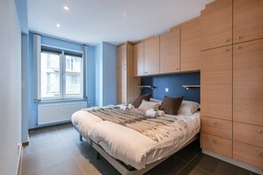 Ein Schlafzimmer mit Bett, Holzschränken, einem Fenster und einer Heizung.