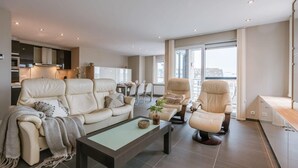 En moderne stue med sofa, lænestole, sofabord og et spiseområde med stole.