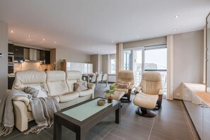 Ein modernes Wohnzimmer mit einer Couch, Sesseln, einem Couchtisch und einem Essbereich mit Stühlen.