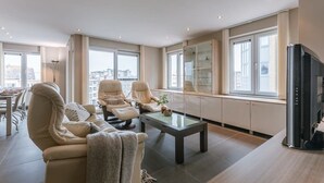 En moderne stue med sofa, lænestole, sofabord og fjernsyn.