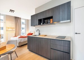 A compact kitchen with dark cabinetry, a central island, and a built-in oven. - Cozy studio w/ workspace (Gent)