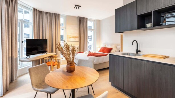 Moderni hotellihuone, jossa on ruokailutila, televisio, sohva ja pieni keittiö.