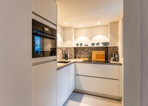 A modern kitchen with white cabinets, a built-in oven, a marble backsplash, and a wooden cutting board. - Pet-friendly Ghent retreat w/ terrace (Gent)