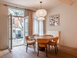 A dining area with a round table, six chairs, a hanging light fixture, a window with curtains, and a framed abstract artwork on the wall. - Pet-friendly Ghent retreat w/ terrace (Gent)