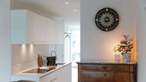 A modern kitchen with white cabinets, a black clock, and a wooden cabinet with a plant. - Beachfront Apt w/Terrace, City View & Fast WiFi (Knokke-Heist)
