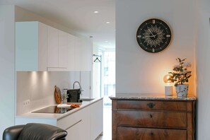 A modern kitchen with white cabinets, a black clock, and a wooden cabinet with a plant. - Beachfront Apt w/Terrace, City View & Fast WiFi (Knokke-Heist)