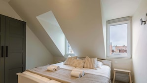 A bedroom with a bed, pillows, a bench, a wardrobe, and a window with a view. - Beachfront Apt w/Terrace, City View & Fast WiFi (Knokke-Heist)