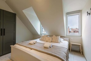 A bedroom with a bed, pillows, a bench, a wardrobe, and a window with a view. - Beachfront Apt w/Terrace, City View & Fast WiFi (Knokke-Heist)