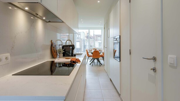 A modern kitchen with a built-in stove, a dining area with a table and chairs, and a view through a window. - Beachfront Apt w/Terrace, City View & Fast WiFi (Knokke-Heist)