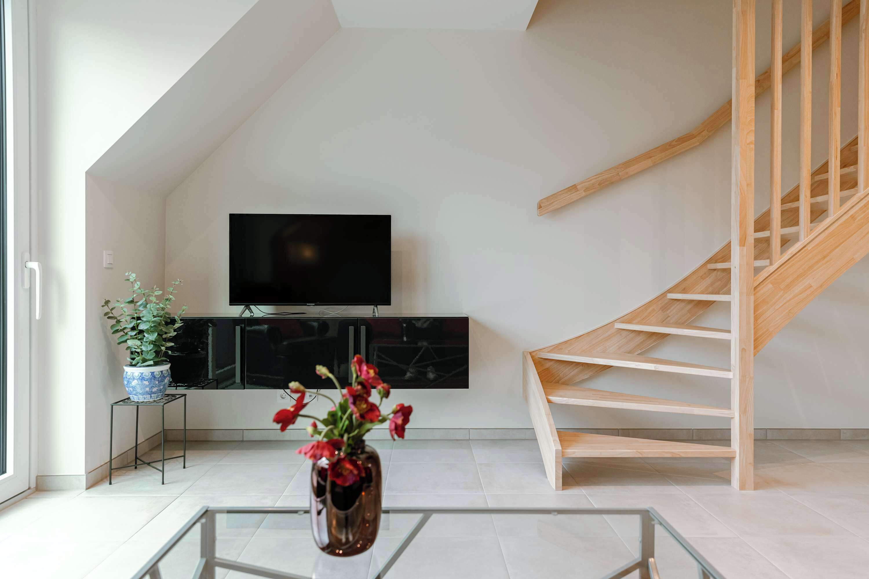 Ein modernes Wohnzimmer mit Fernseher, einem Blumentopf, einer Vase mit Blumen und einer Holztreppe.