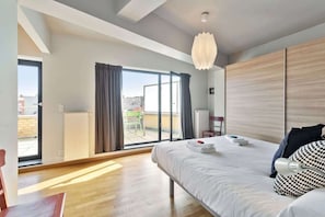 Ein modernes Hotelzimmer mit einem großen Bett, einer Deckenleuchte, Blick durch eine Schiebetür in einen Außenbereich und einem Heizkörper an der Wand.