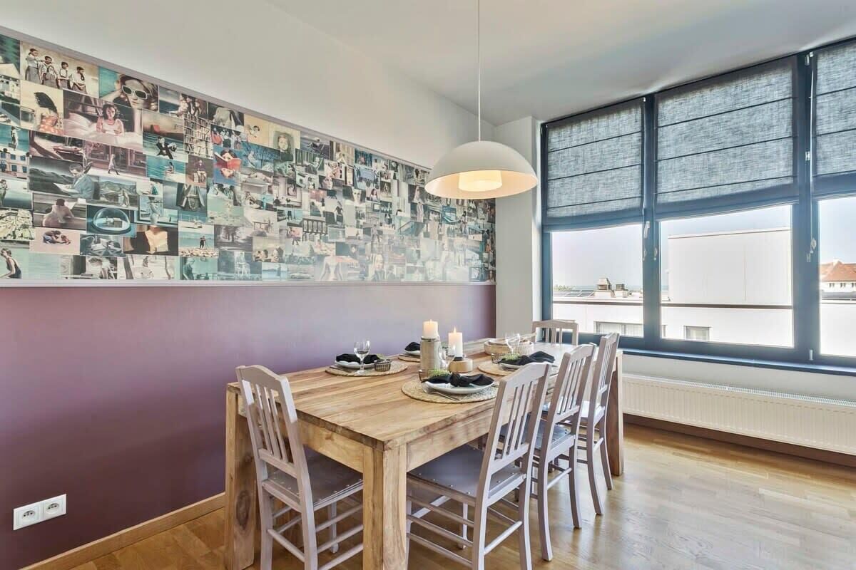 A dining area with a wooden table, white chairs, a wall collage, and a large window.