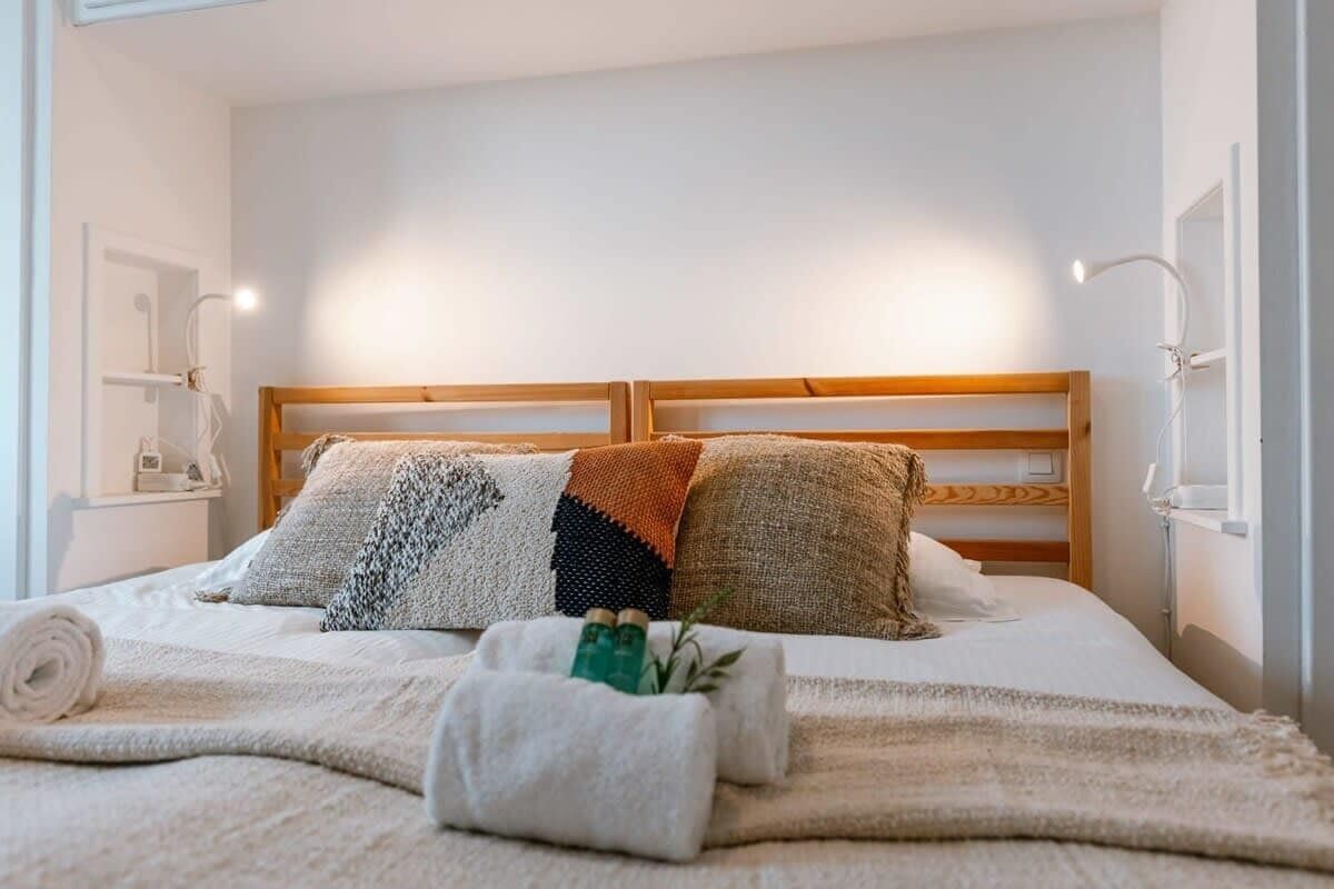 Een net opgemaakt bed met een houten hoofdbord, een witte deken en een opgerolde handdoek.