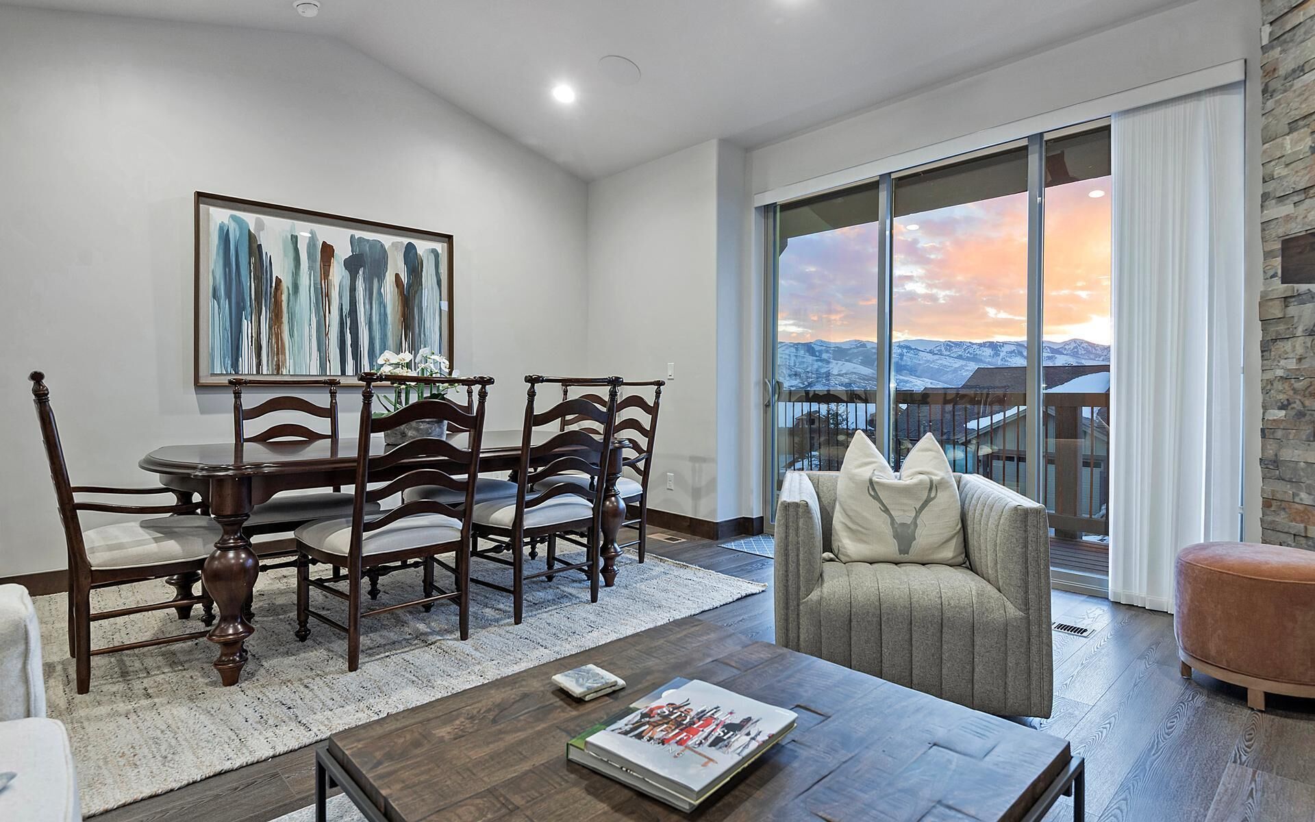 A dining area with a table and chairs, a sofa, and a large window with a view of mountains.