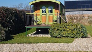 A small, single-story building with a curved roof, a balcony with a railing, and a gravel path leading to it.