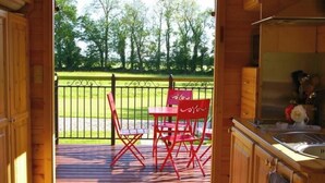 A wooden cabin interior with a balcony, a dining table, and red chairs.