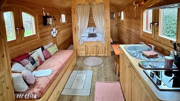 A cozy wooden cabin interior with a bed, a small sofa, a dining area, and a sink.