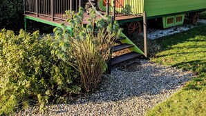 A green and orange train car with a covered porch and a small deck.