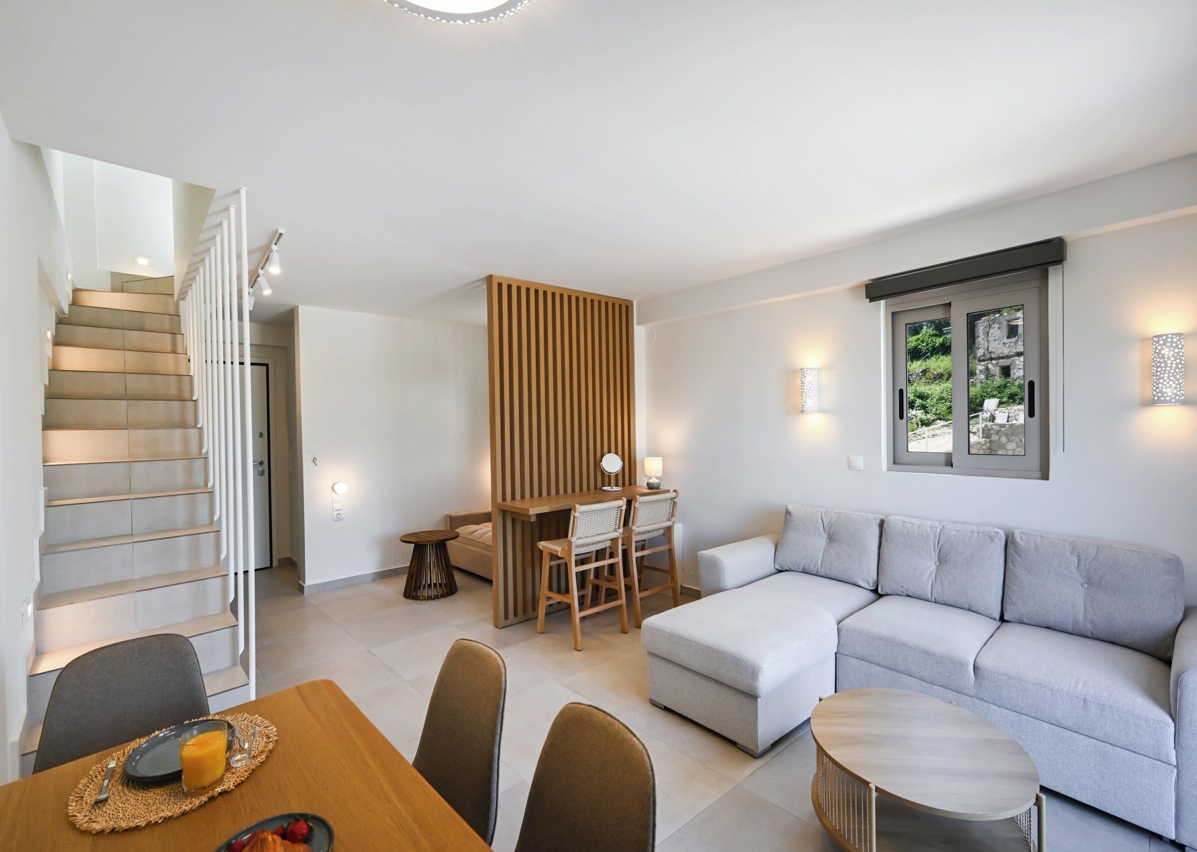 A modern living room with a staircase, a dining area, and a seating area with a view of the outdoors.