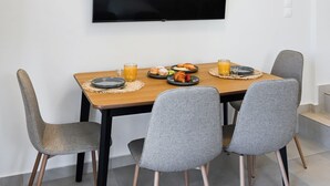 A dining area with a table, chairs, a flat-screen TV, and a breakfast setting. - Azure II Suite (Lefkada)