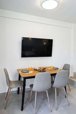 A dining area with a table, chairs, a flat-screen TV, and a breakfast setting. - Azure II Suite (Lefkada)