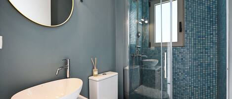 A modern bathroom with a large white sink, a toilet, and a glass-enclosed shower.