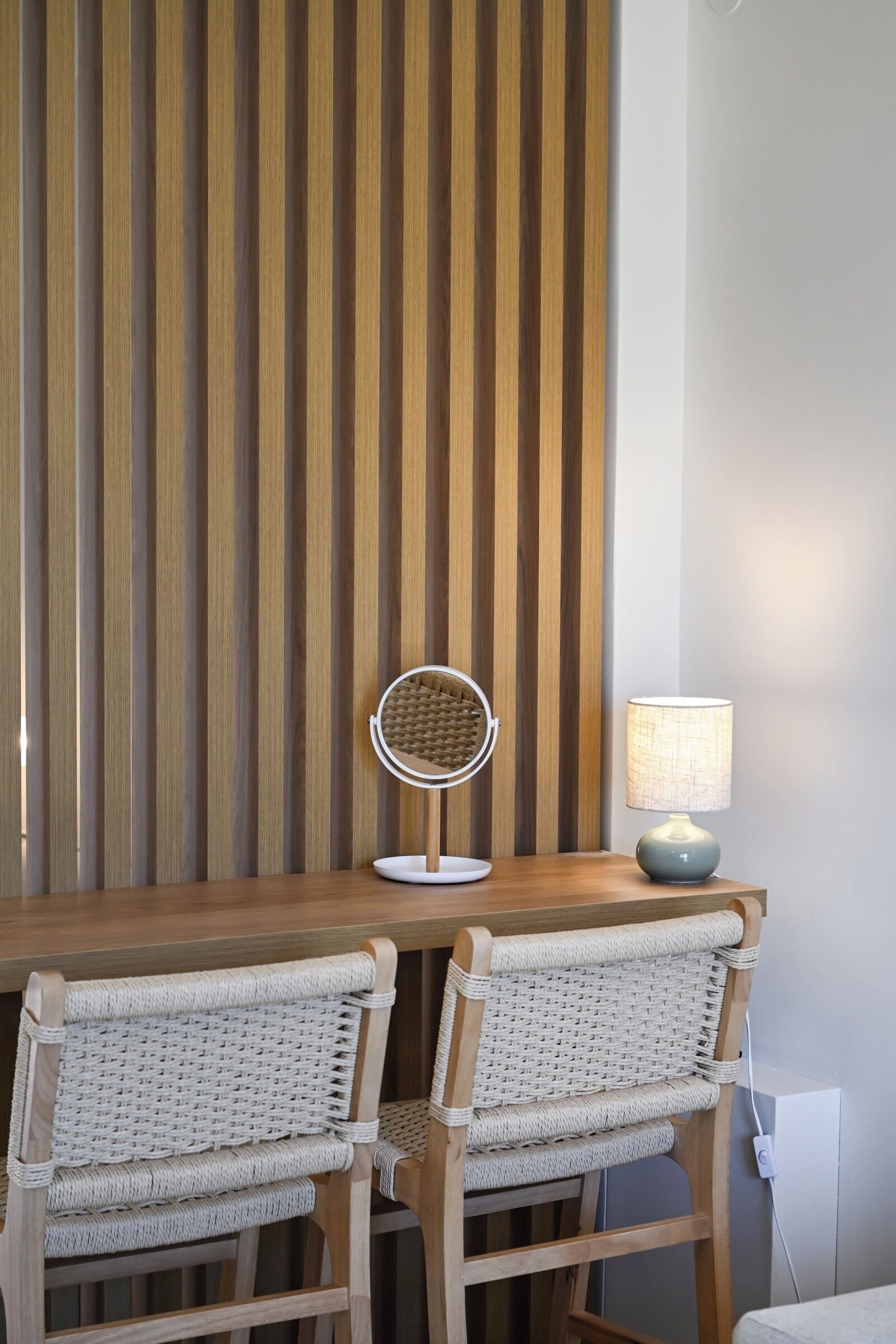 Une table en bois, deux chaises en osier, un miroir rond et une lampe.