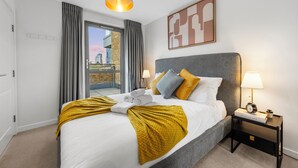Quarto de hotel com cama, mesa de cabeceira, abajur, quadro emoldurado e vista para o exterior.