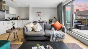 Uma sala de estar moderna com um sofá cinzento, uma mesa de centro com uma planta e vista para o exterior.