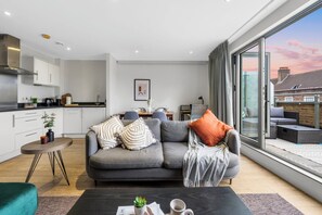 A modern living room with a grey sofa, a coffee table with a plant, and a view of the outside. - Central London Skyline Retreat | Private Terrace Near Big Ben (London)