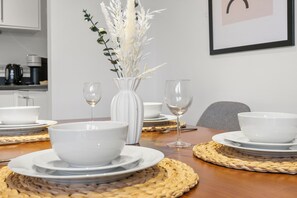A dining table set with white bowls and wine glasses, a vase with white flowers, and a woven placemat. - Central London Skyline Retreat | Private Terrace Near Big Ben (London)