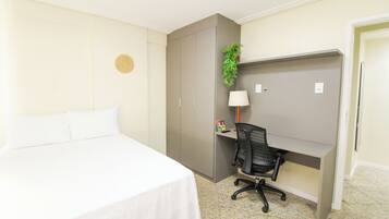 A hotel room with a bed, a desk, a chair, a plant, and a wall decoration.