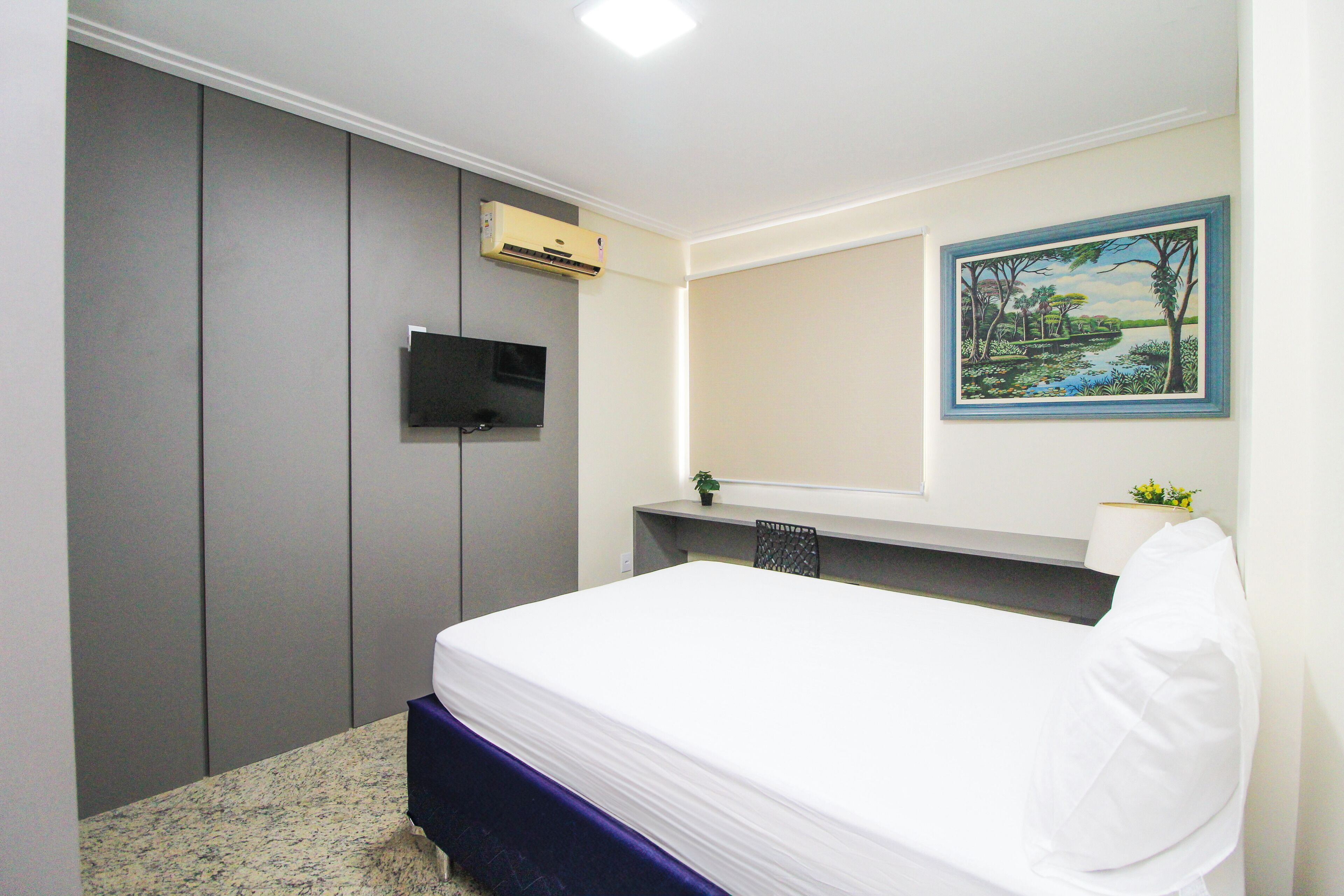 A bedroom with a bed, a TV, a painting, and a desk with a chair.