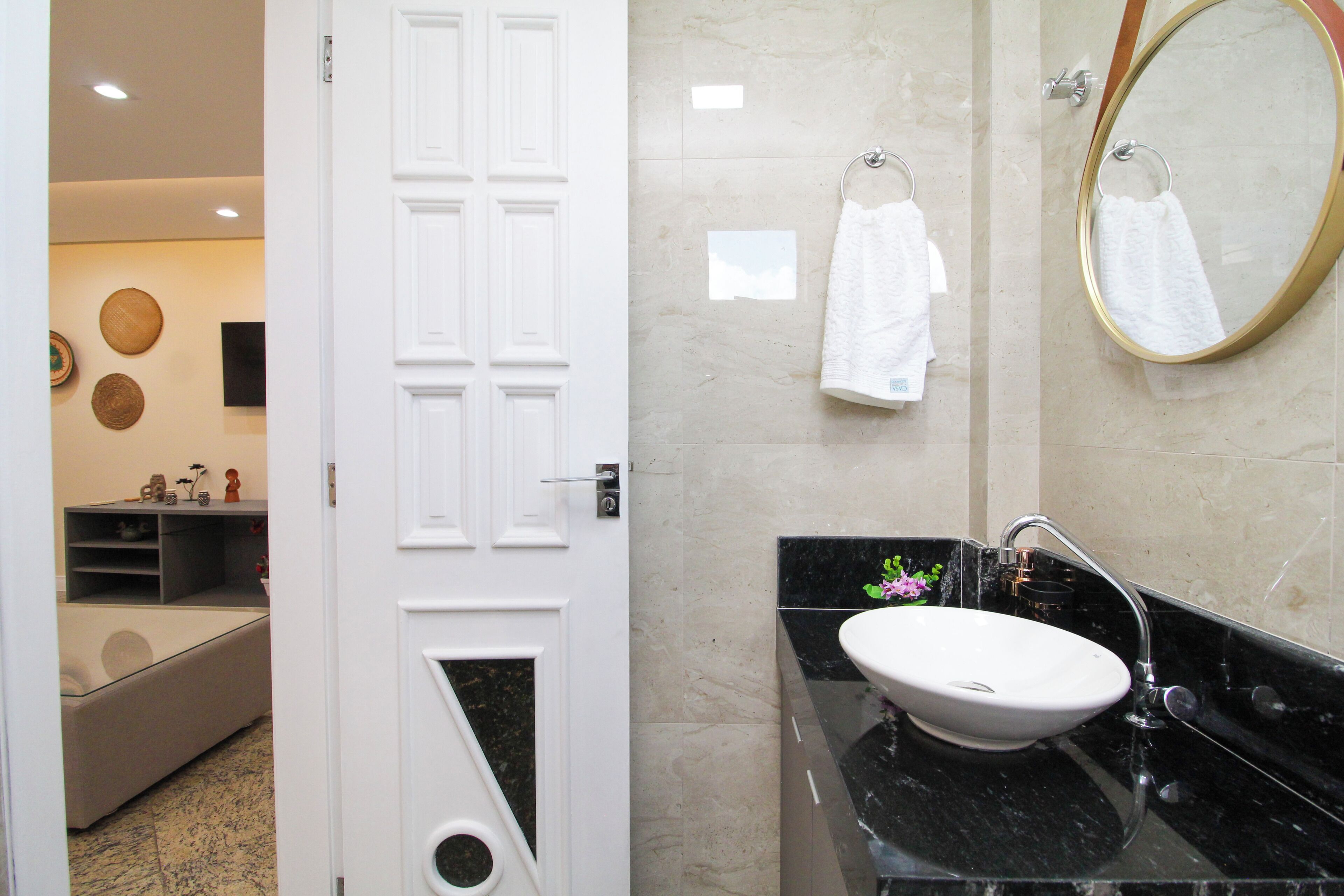 A bathroom with a white door, a sink, a mirror, and towels on the wall.