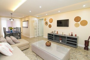 Uma sala de estar com sofá, mesa de centro, televisão e uma parede decorada.