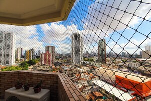 Um edifício alto com vista através de uma cerca de arame, apresentando várias varandas e uma parede de tijolos.