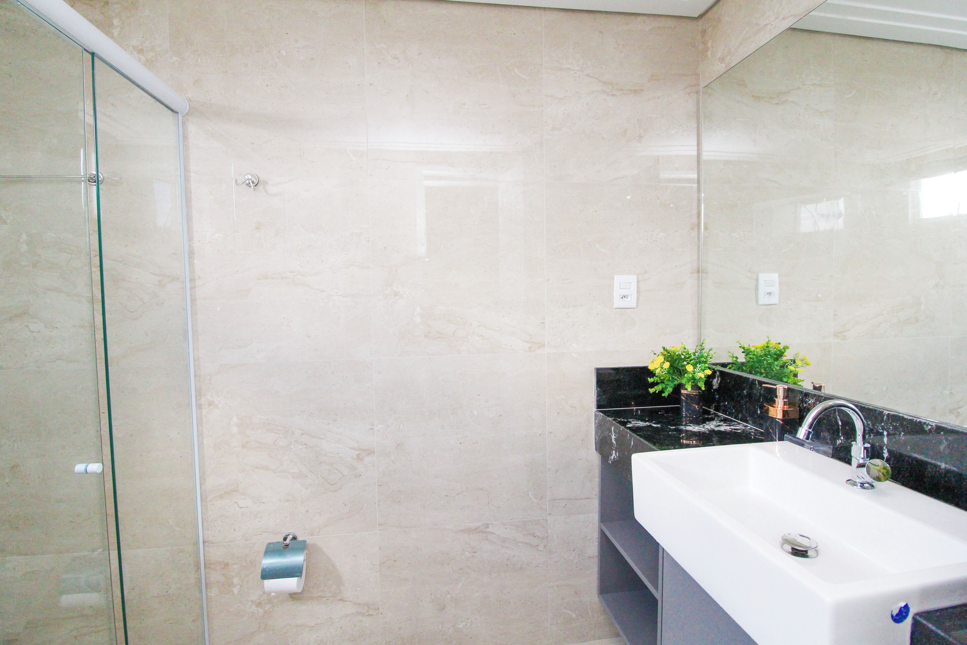 A bathroom with a glass shower enclosure, a white sink with a black countertop, and a mirror.
