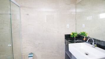 A bathroom with a glass shower enclosure, a white sink with a black countertop, and a mirror.
