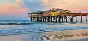 A wooden pier leading to a yellow building with a balcony overlooking the ocean. - SunGlow 807 (Daytona Beach Shores)