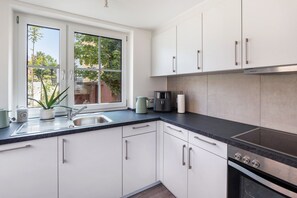 A modern kitchen with white cabinets, a black countertop, and a window overlooking a garden. - Apartment at the Fountain (Schrozberg)