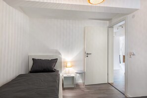A bedroom with a bed, a bedside table with a lamp, and a door leading to another room. - Apartment at the Fountain (Schrozberg)