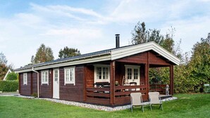 A wooden cabin with a porch, a chimney, and a small garden area. - 4 Star Holiday Home in Stege (Stege)