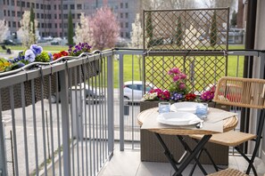 Een balkon met een rieten tafel voor twee personen, een rieten stoel en een metalen hekwerk.
